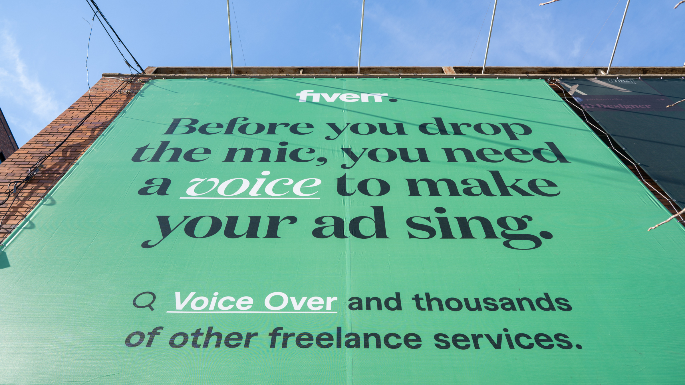 Urban street scene: roof-mounted billboards and wheat-pasted posters on brick, parked car, ONE WAY sign—voice-over, brand bible, service cards, and Fiverr logo treatments