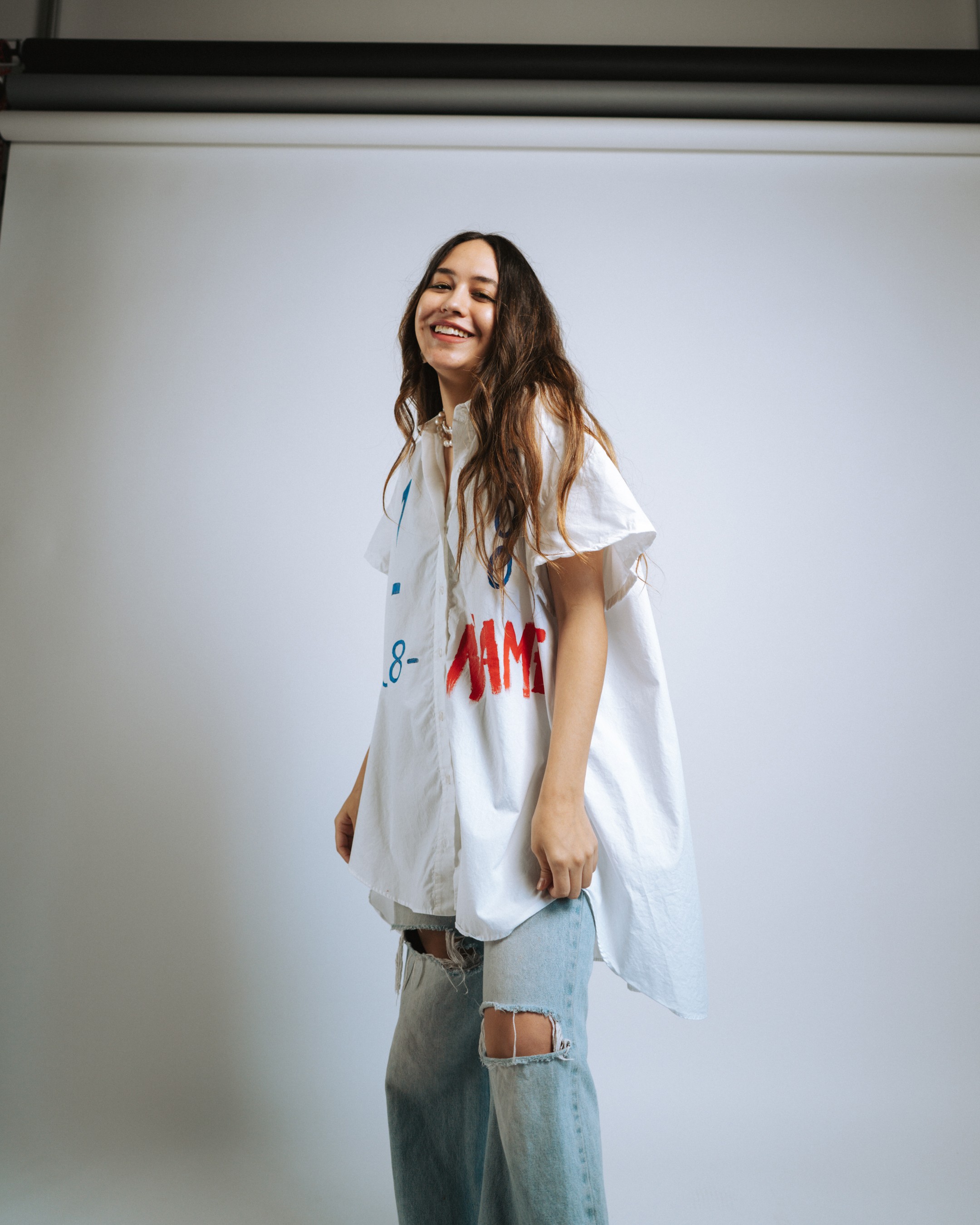 Street scene: laughing model at a green post, split red-and-black sweatshirt with graphic center, city brick and traffic light behind, YOUR NAME badges